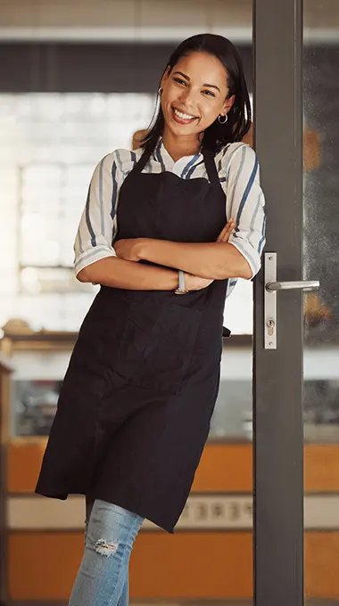 shop-owner-iStock-1400817945 photo of a smiling female business owner standing at the door to her shop
